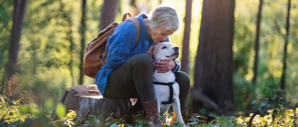 A woman sitting with her dog on a hike in the woods