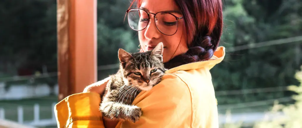 A woman carrying a cat over her shoulder